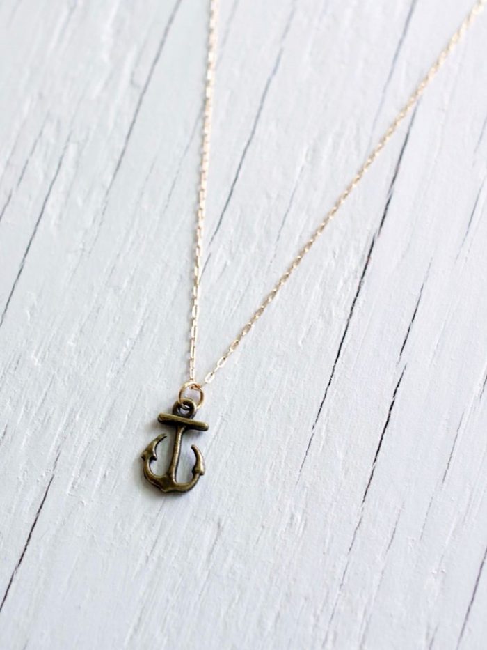 Gold anchor necklace on a 14kt gold fill chain laying on a white wood background
