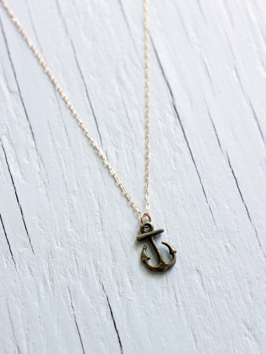 Sailor anchor necklace in brass on a gold chain laying on a white wooden background