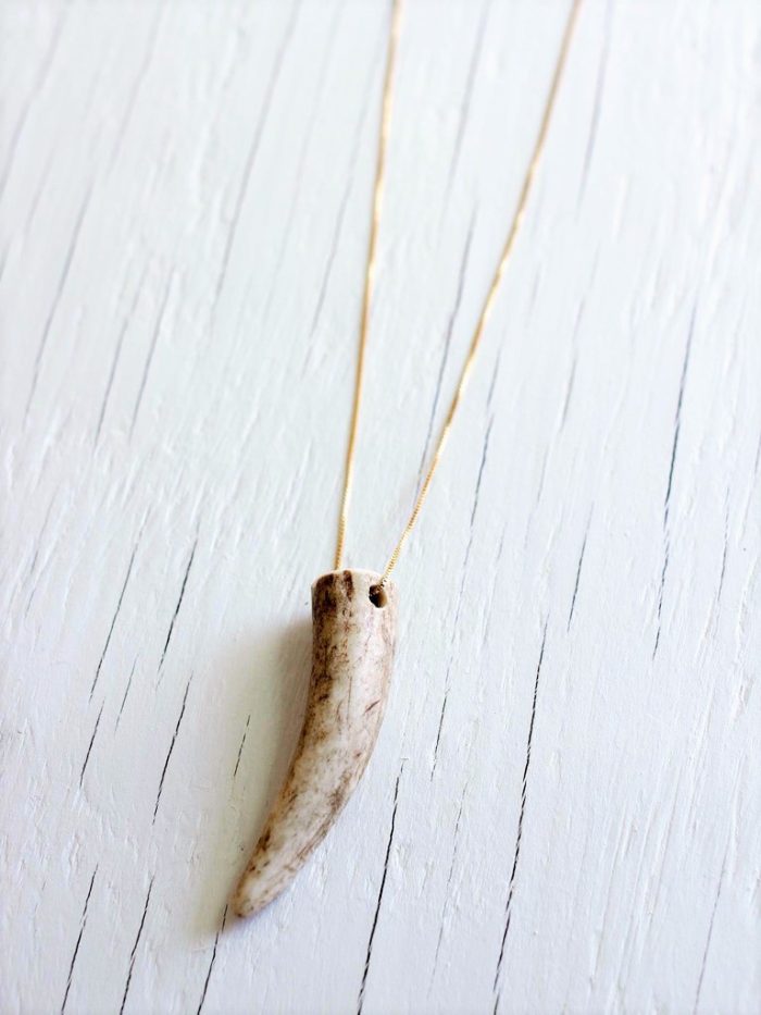 Deer antler necklace strung on a 14kt gold fill chain laying on top of a white wood backgrund