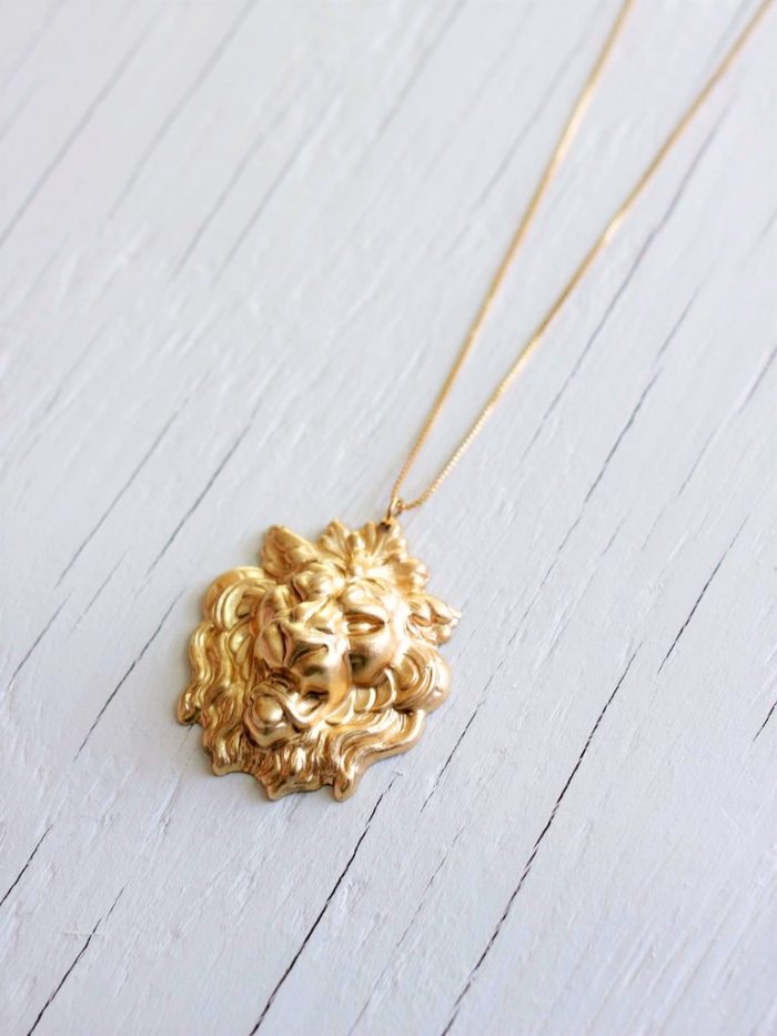 gold lion necklace with a lion head brass pendant on a 14kt gold fill box chain laying on a white wood background
