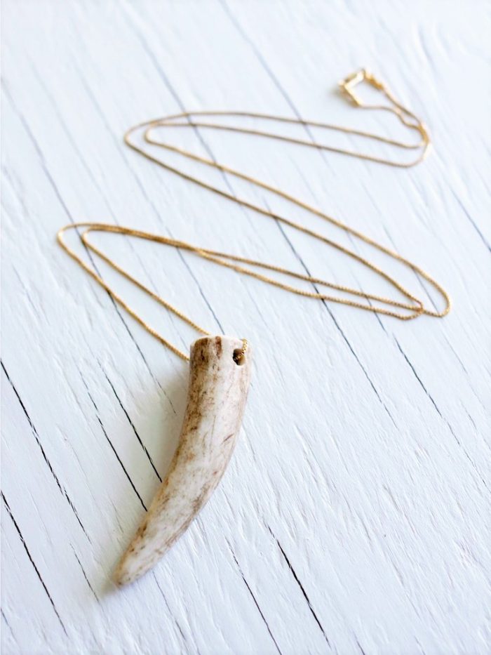 Deer antler necklace strung on a 14kt gold fill chain laying on top of a white wood backgrund
