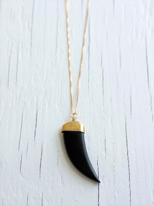 matte black and gold pendant necklace strung from a gold chain on a white wooden background