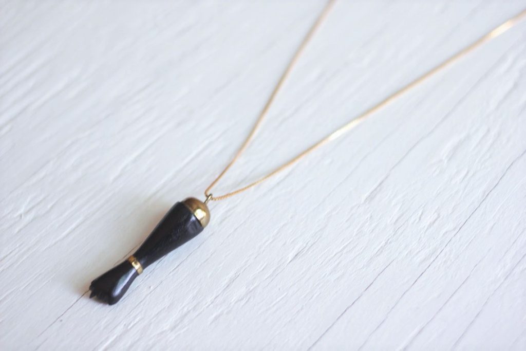 Black figa arm pendant strung on gold chain necklace laying on top of white wooden background