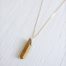 Quartz necklace dipped in gold strung on a 14kt gold fill box chain laying on a white wood background