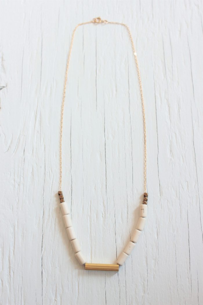 Delicate beaded necklace with brass bar on a white wood background