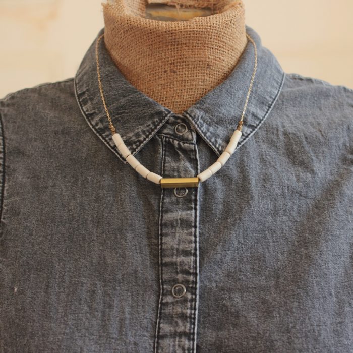 Minimalist white bead and gold necklace on a mannequin wearing a gray button down shirt