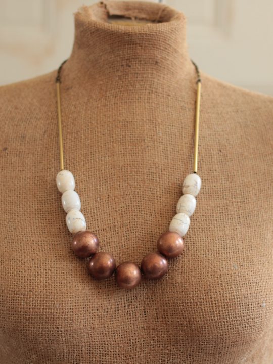 Mannequin wearing a copper ball necklace in front of a white wall