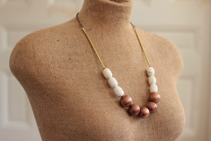 Mannequin wearing a copper ball necklace in front of a white wall