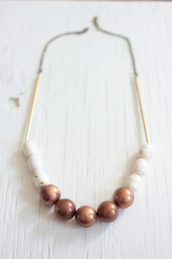 Statement necklace made with copper balls, white magnesite stone barrels strung on a raw brass chain laying on a white wood table