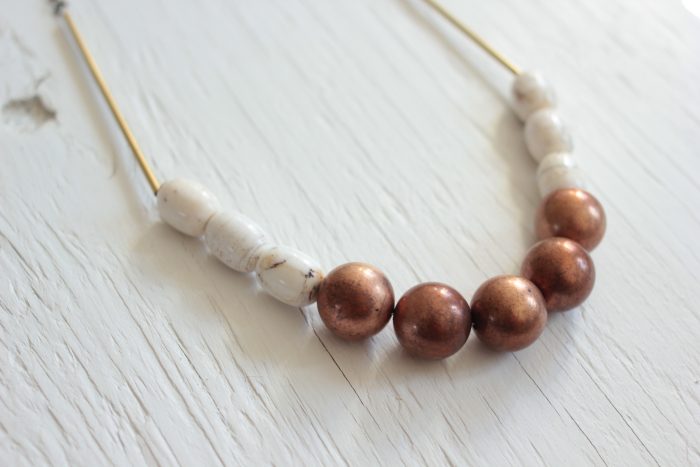 Statement necklace made with copper balls, white magnesite stone barrels strung on a raw brass chain laying on a white wood table