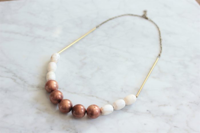 Statement necklace made with copper balls, white magnesite stone barrels strung on a raw brass chain laying on a white marble table